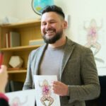 Happy male teacher with poster of frog internal structure looking at student