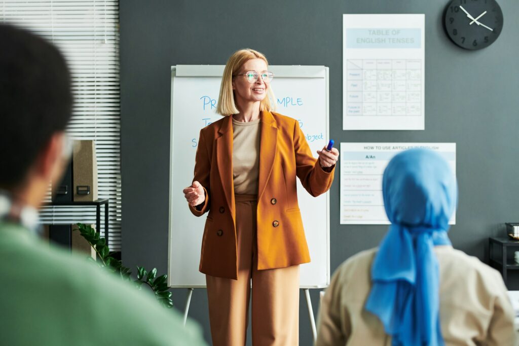 Happy mature blond teacher or speaker standing in front of audience